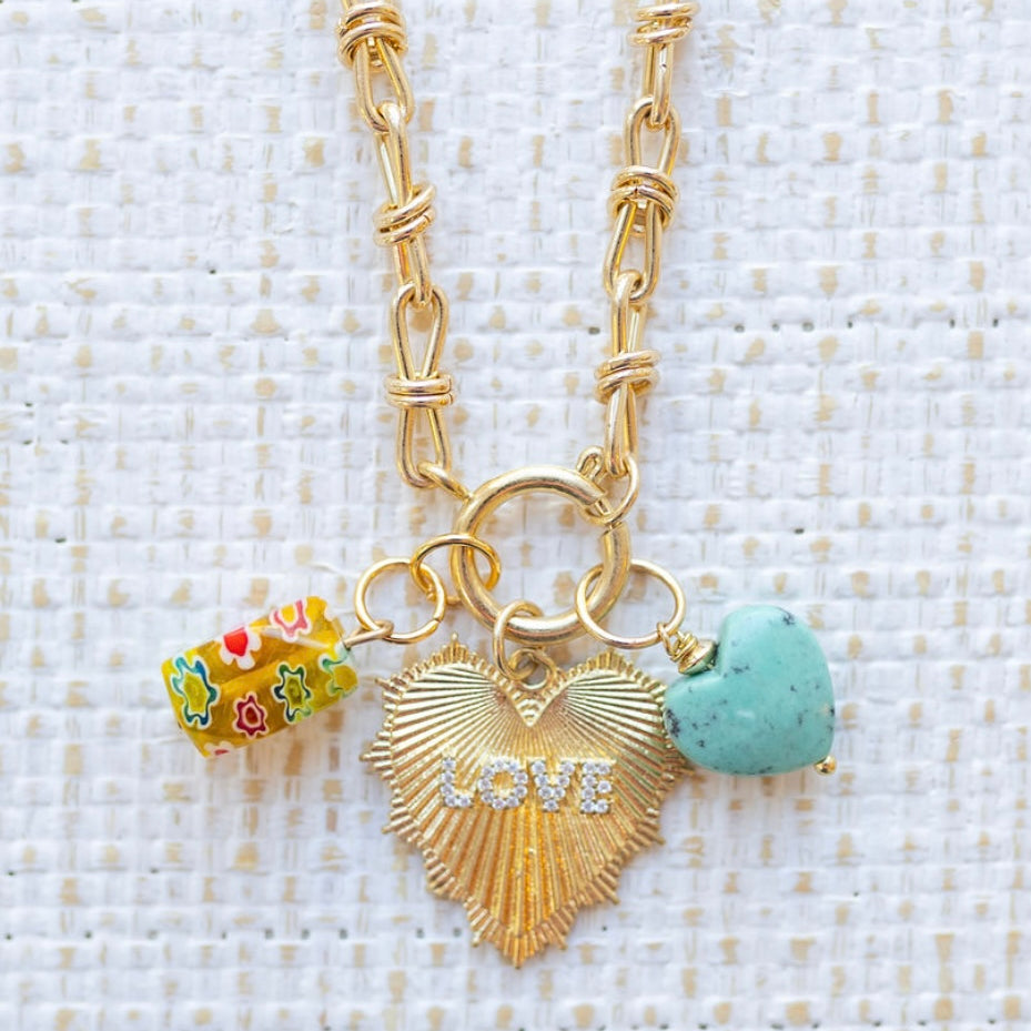 Picture of gold toggle chain with a large gold heart pendant with the word "Love" in diamonds and a yellow flowered charm and blue turquoise heart charm.