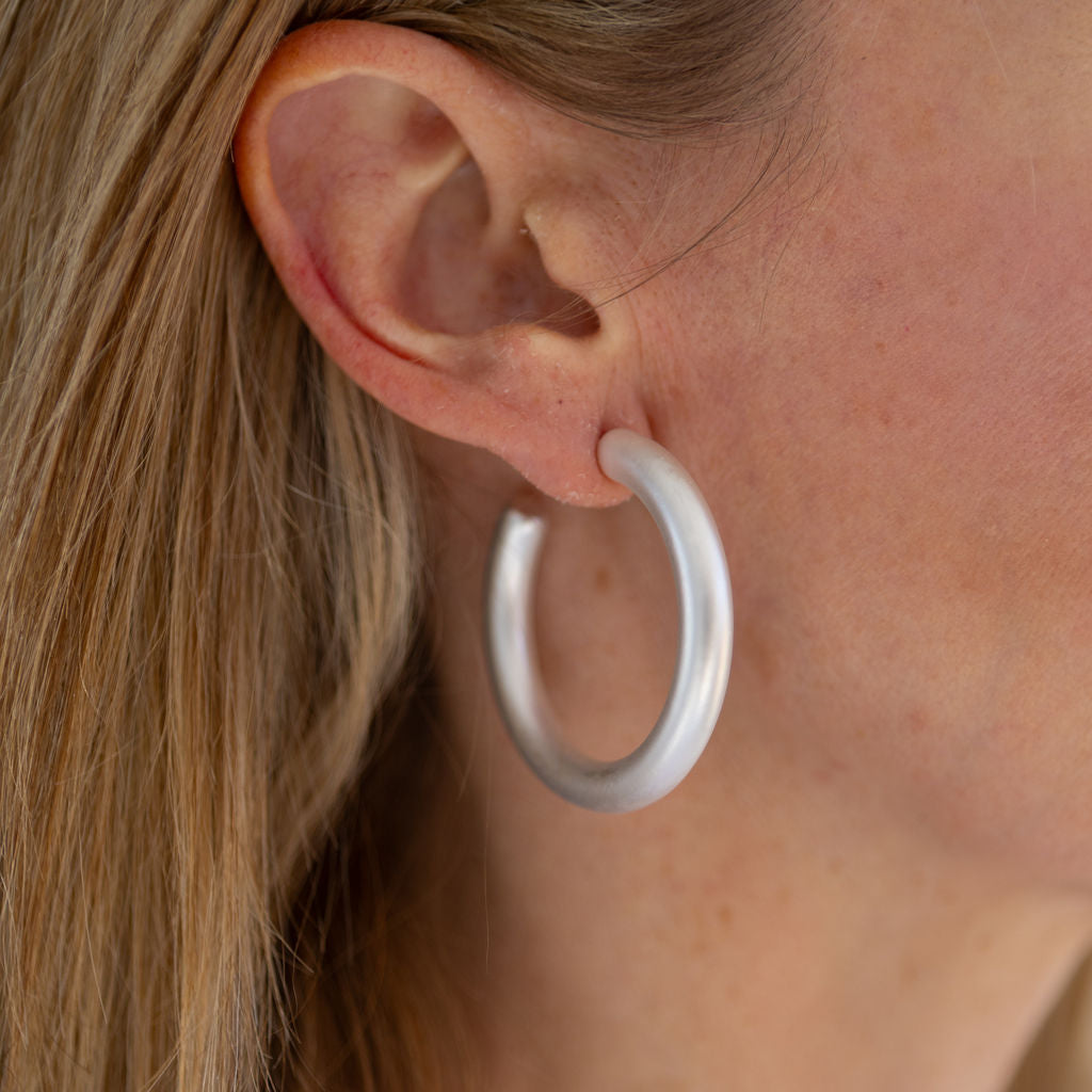 A close-up image of a woman's ear wearing a silver hoop earring.