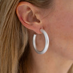 A close-up image of a woman's ear wearing a silver hoop earring.