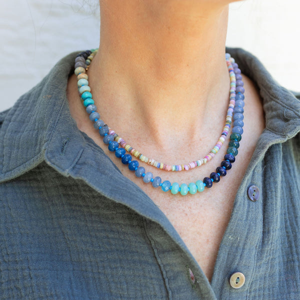 Woman in a green collared shirt wearing two necklaces: one wit smaller colorful beads and another with bigger different blue colored beads 