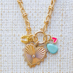 Picture of gold toggle chain with a large gold heart pendant with a diamond at center and several charms. Charms include a gold horseshoe, turquoise tear drop and small pink heart.
