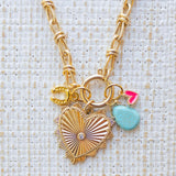 Picture of gold toggle chain with a large gold heart pendant with a diamond at center and several charms. Charms include a gold horseshoe, turquoise tear drop and small pink heart.