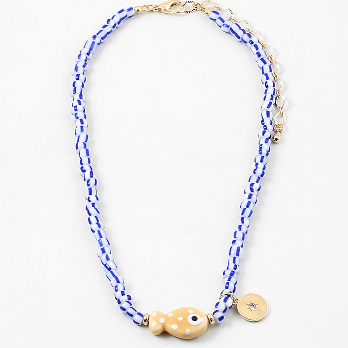 Picture of a bead necklace made of white and blue striped beads and a tan fish bead with a gold disc pendant.