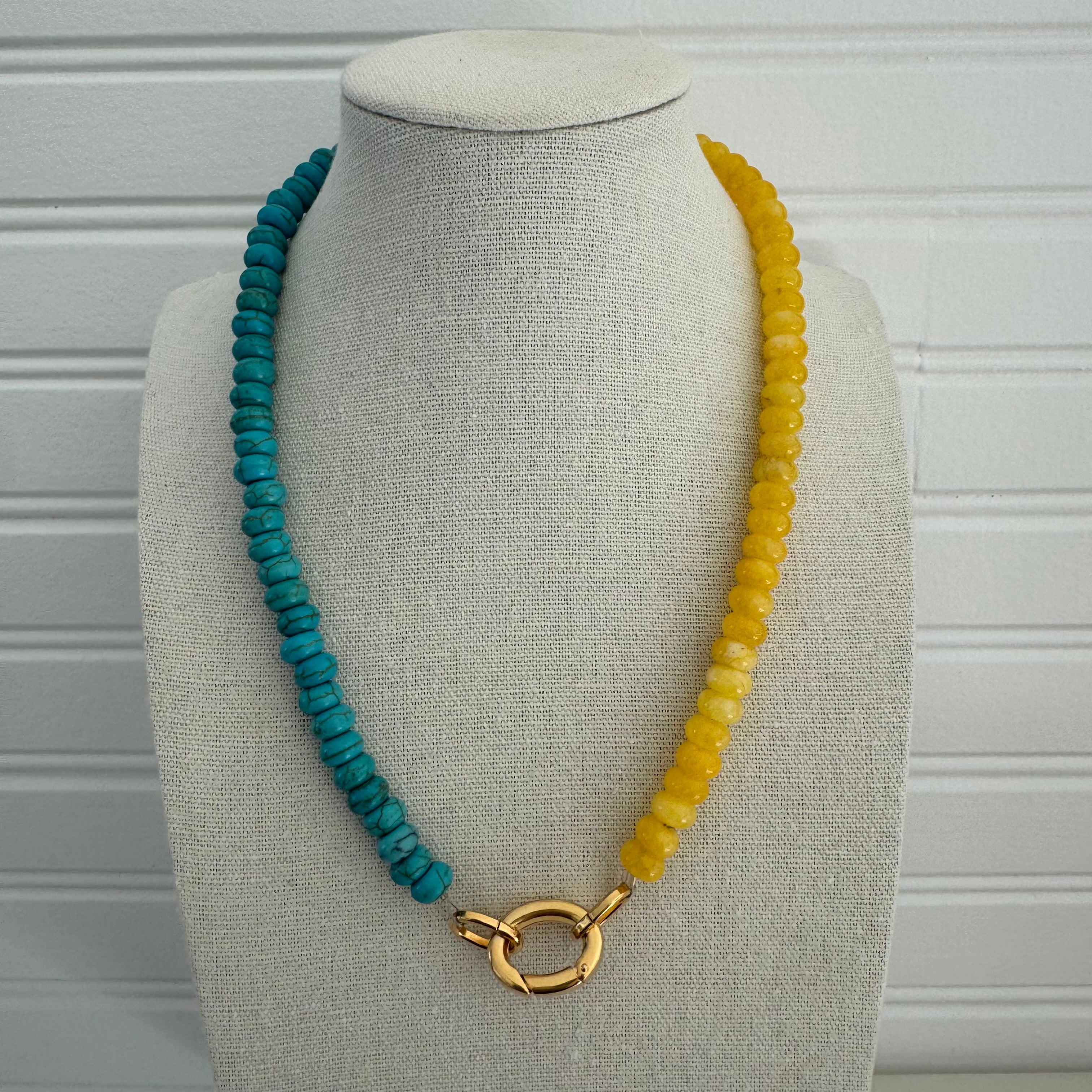Picture of a bead necklace made of half of turquoise beads and bold yellow. The necklace has a large gold carabiner accent clasp.