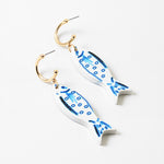 Picture of small gold hoops with white fish with blue details hanging from them.
