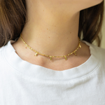 Girl wearing a gold necklace with a thin chain and little gold rectangles attached to it around her neck