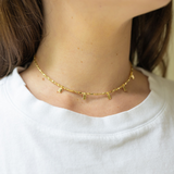 Girl wearing a gold necklace with a thin chain and little gold rectangles attached to it around her neck