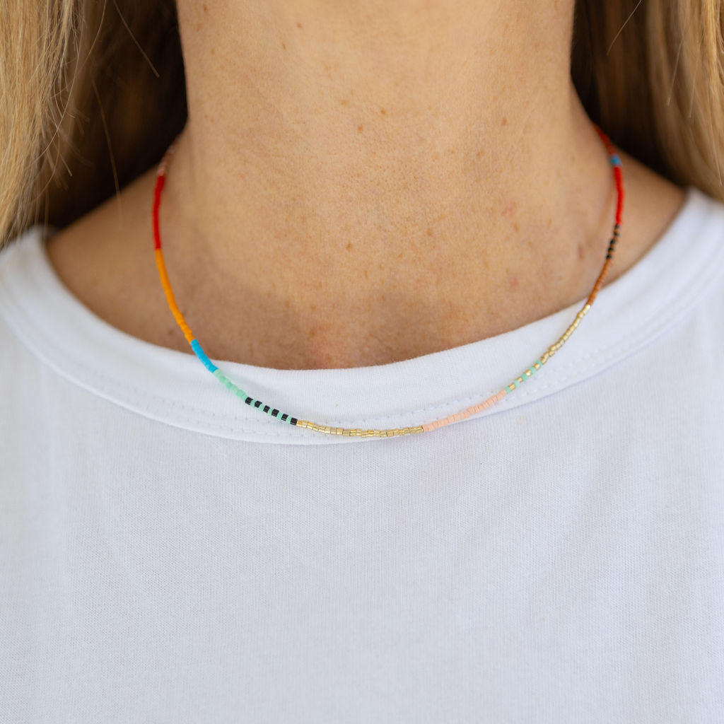 A person wearing a white t-shirt modeling a beaded necklace with a pattern of primary colored beads.