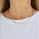 A person wearing a white t-shirt modeling a beaded necklace with a pattern of primary colored beads.