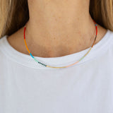 A person wearing a white t-shirt modeling a beaded necklace with a pattern of primary colored beads.