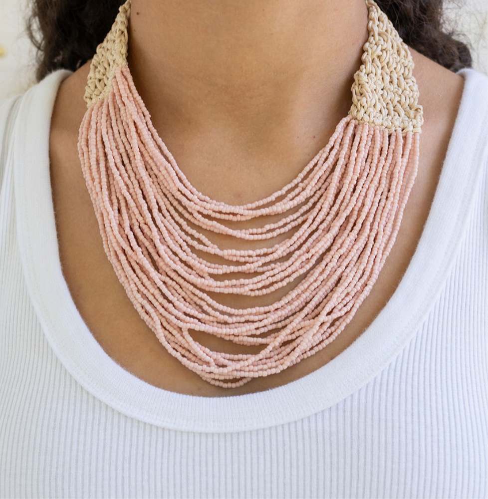 Necklace with multi-strand pink beads and beige crochet clasp worn by a person on a white background