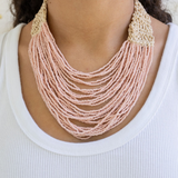 Necklace with multi-strand pink beads and beige crochet clasp worn by a person on a white background