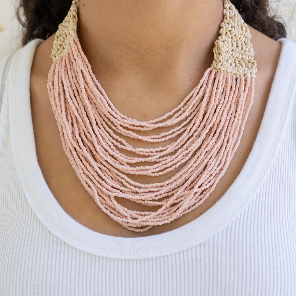 Necklace with multi-strand pink beads and beige crochet clasp worn by a person on a white background