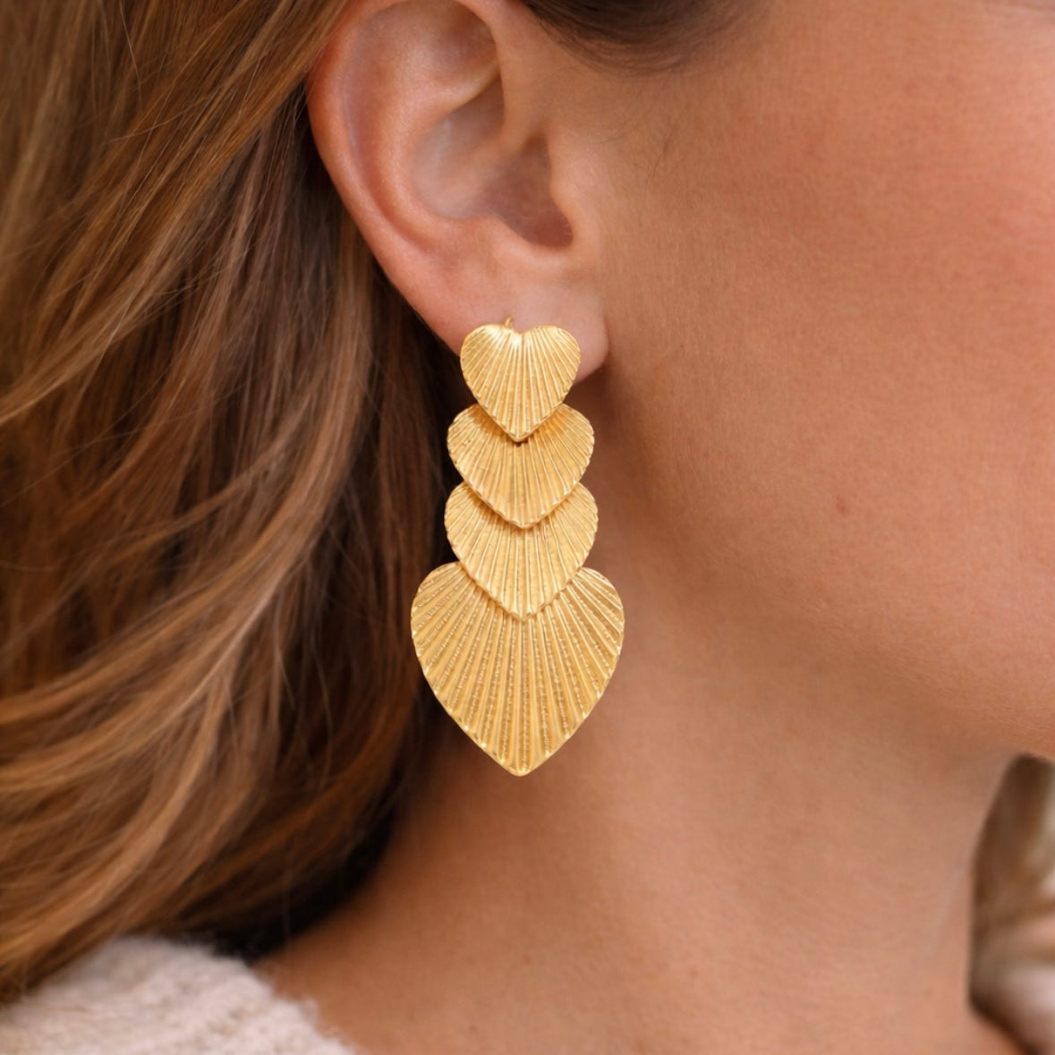 Gold, textured heart-shaped earrings worn by a person with brown hair.