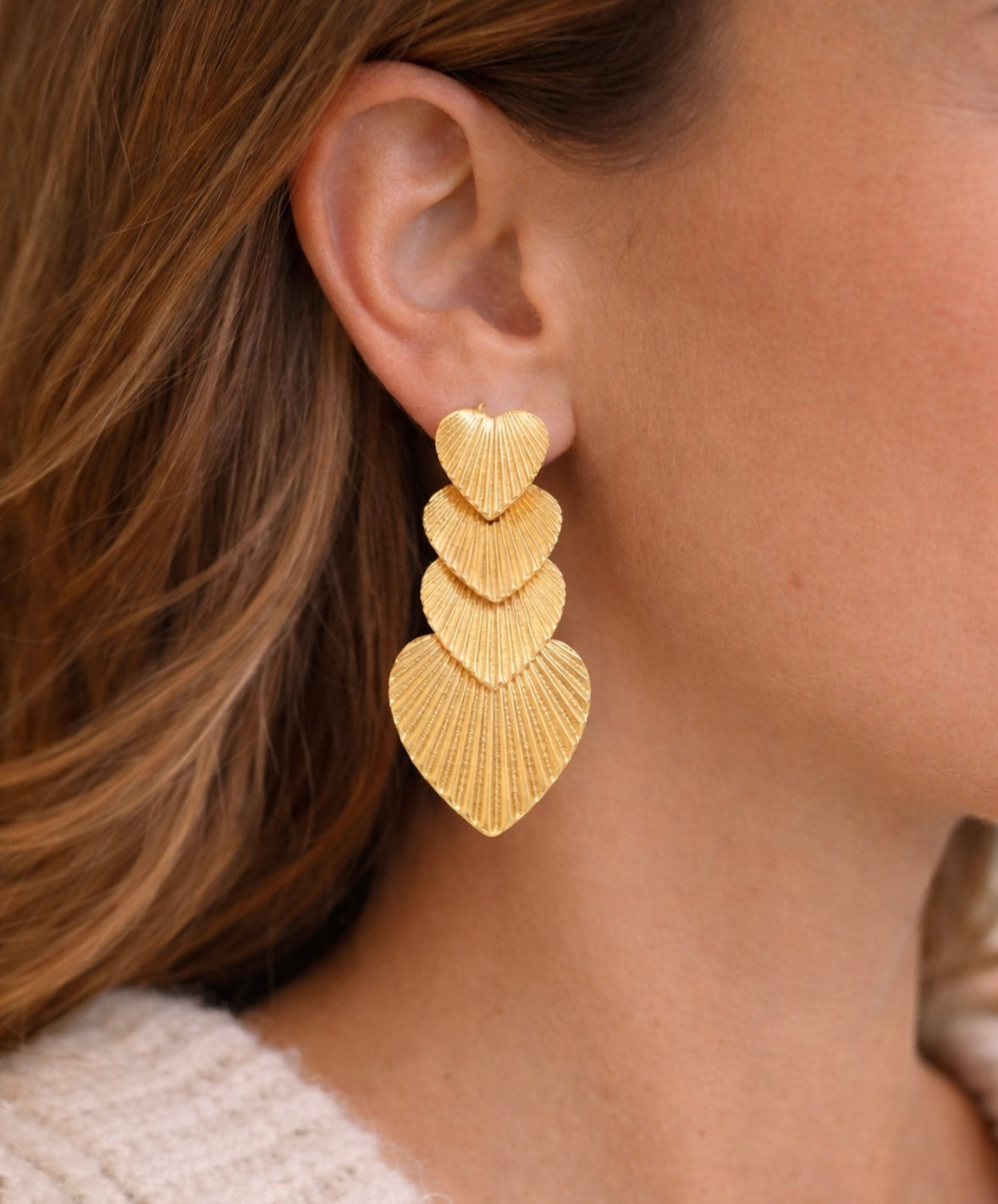 Gold, textured heart-shaped earrings worn by a person with brown hair.