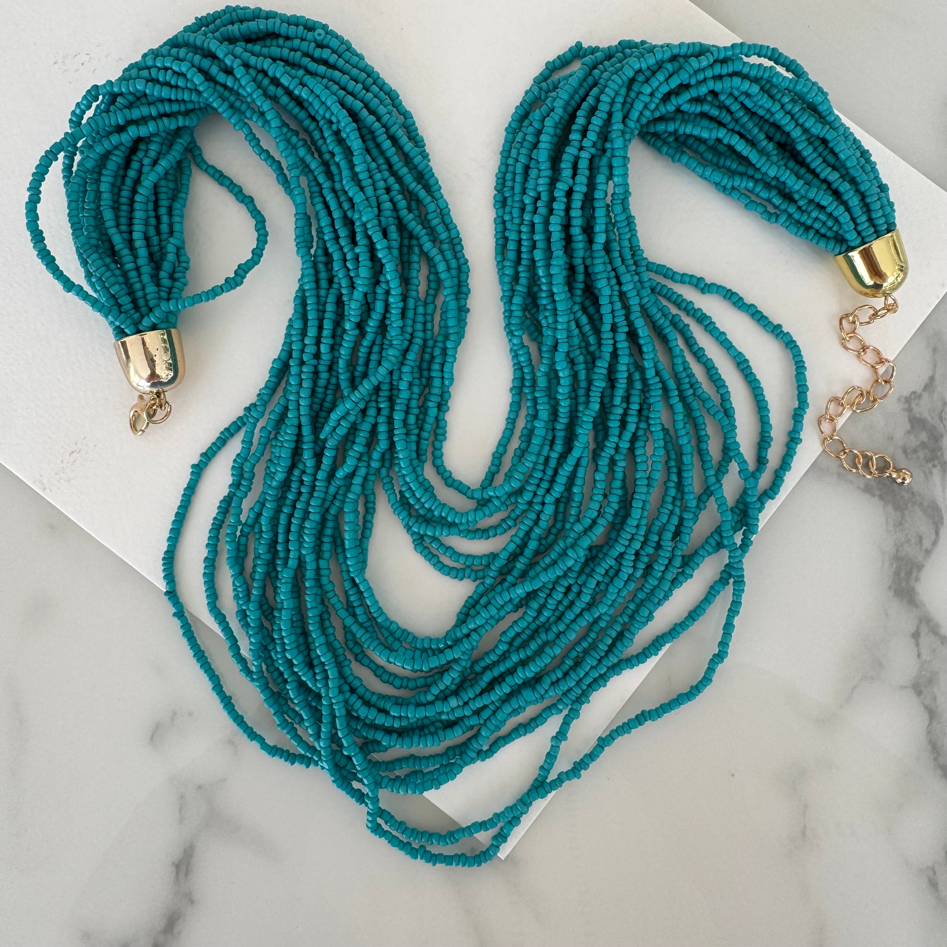 Picture of a necklace made out of multiple strands of teal beads with a large gold clasp.
