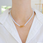 Model wearing a white bead necklace with a large gold carabiner clasp at its center.