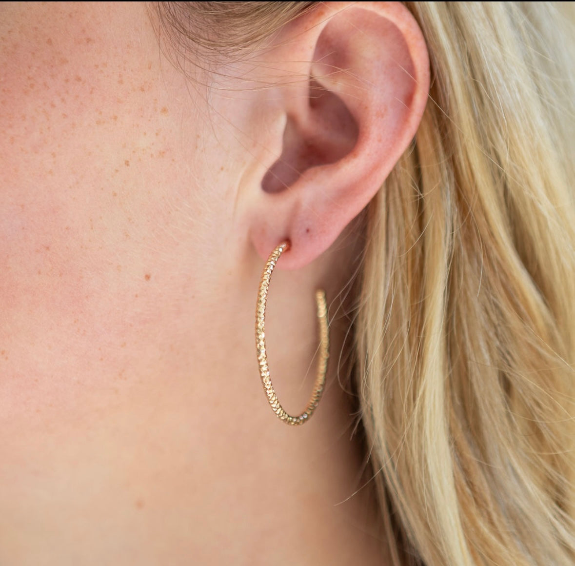 Textured gold hoop earrings worn by a person with blonde hair.