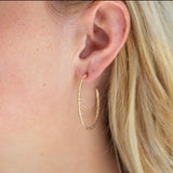 Textured gold hoop earrings worn by a person with blonde hair.