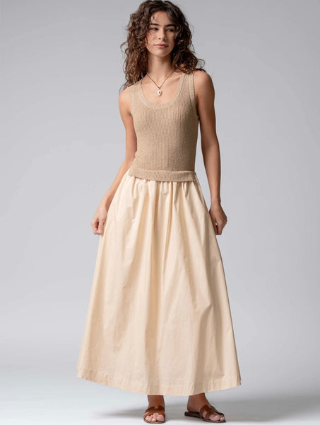 Woman wearing a beige sleeveless top and long skirt against a gray background