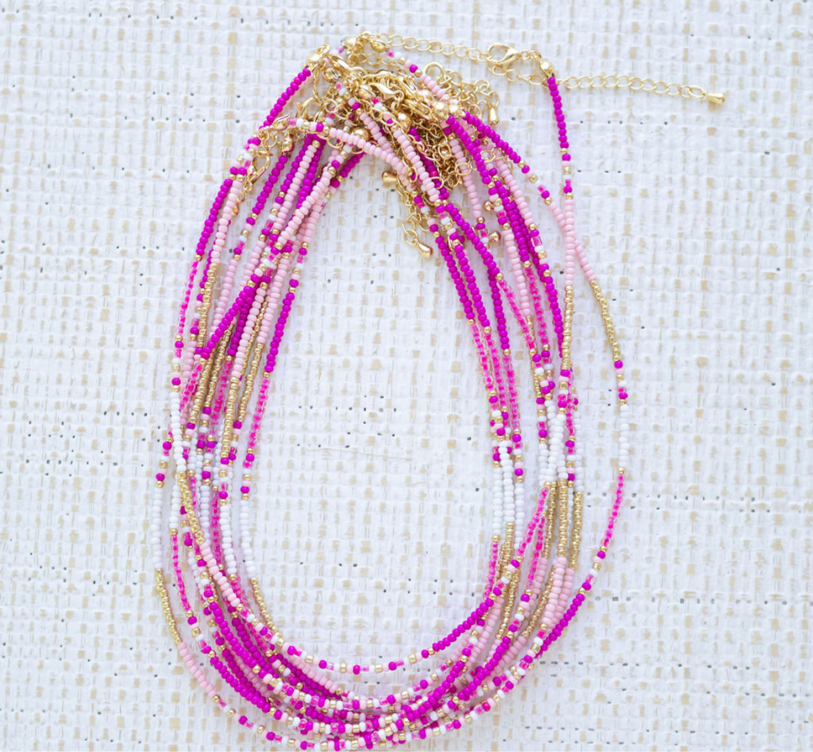 Stack of necklaces with pink and gold beads on a textured white background