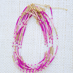 Stack of necklaces with pink and gold beads on a textured white background