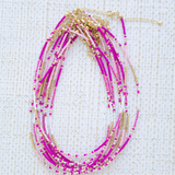 Stack of necklaces with pink and gold beads on a textured white background