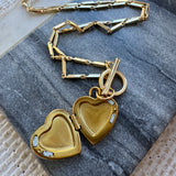Gold heart-shaped locket with chain on a textured surface