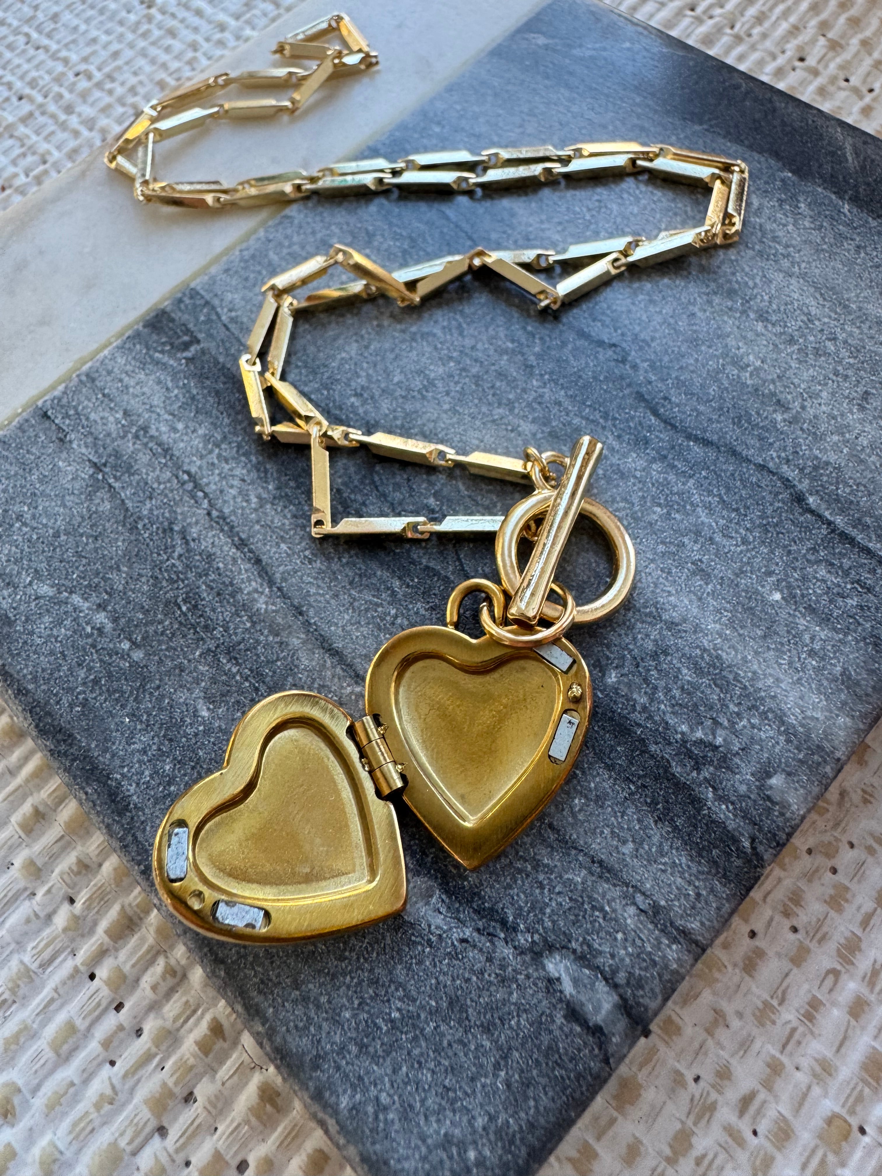 Gold heart-shaped locket with chain on a textured surface