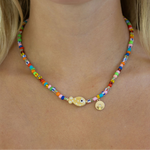 Multicolor bead necklace with a central fish pendant and gold disc pendant.
