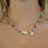 Multicolor bead necklace with a central fish pendant and gold disc pendant.