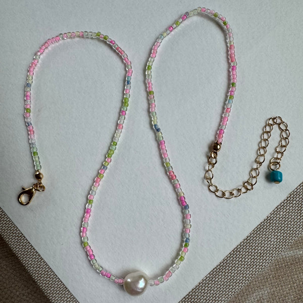 Picture of a delicate seed bead necklace with clear pink, greens and white beads. Center of necklace is a large freshwater Pearl.