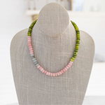 A beaded gemstone necklace displayed on a mannequin, featuring shades of green and pink.
