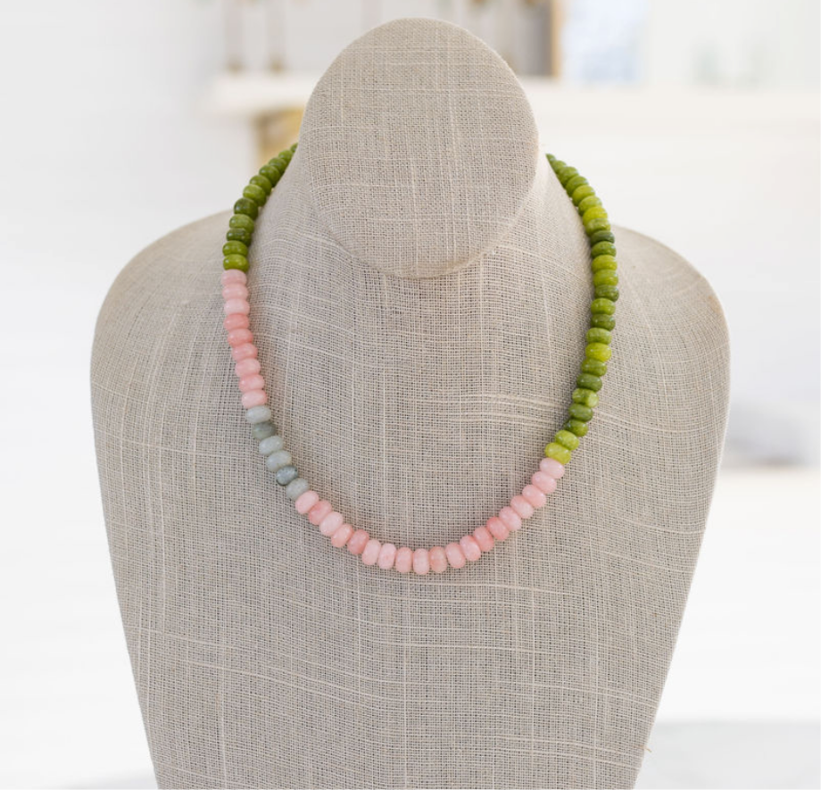 A beaded gemstone necklace displayed on a mannequin, featuring shades of green and pink.