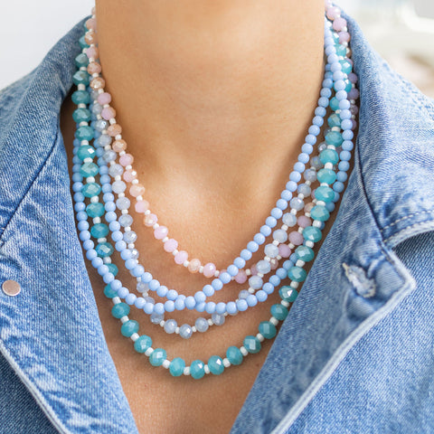 Woman wearing around her neck layered beaded necklaces of purple, pink, and blue