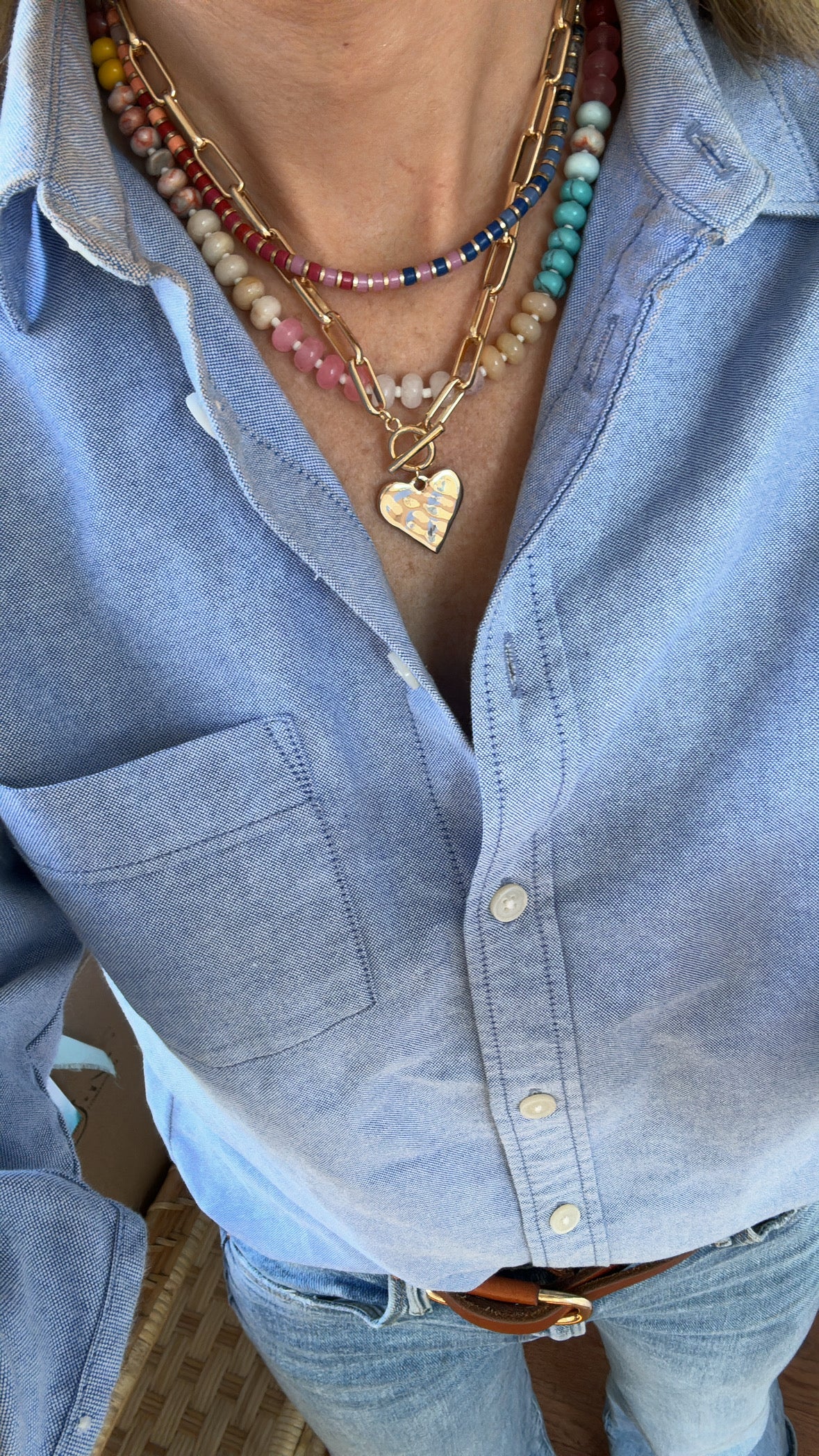 Picture of a woman wearing a layered necklace stack with a bead necklace a  gold link necklace and hammered Heart pendant and small bead necklace.