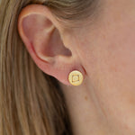 A close-up image of a person wearing a gold-colored stud earring.