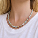 Necklace with multicolored earthy toned beads worn by a person in a white t-shirt.