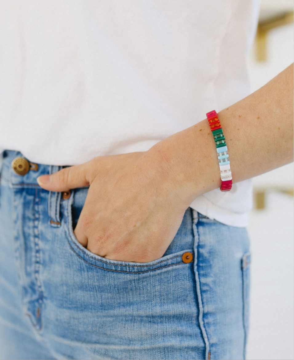 Picture of a woman with her hand in her pocket. She is wearing a beaded bracelet in red, greens, blues and whites.