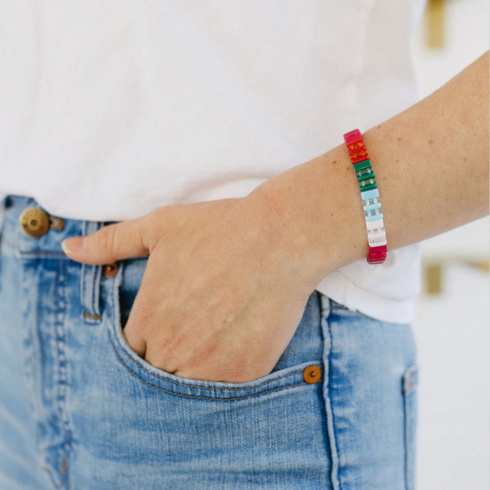 Picture of a woman with her hand in her pocket. She is wearing a beaded bracelet in red, greens, blues and whites.