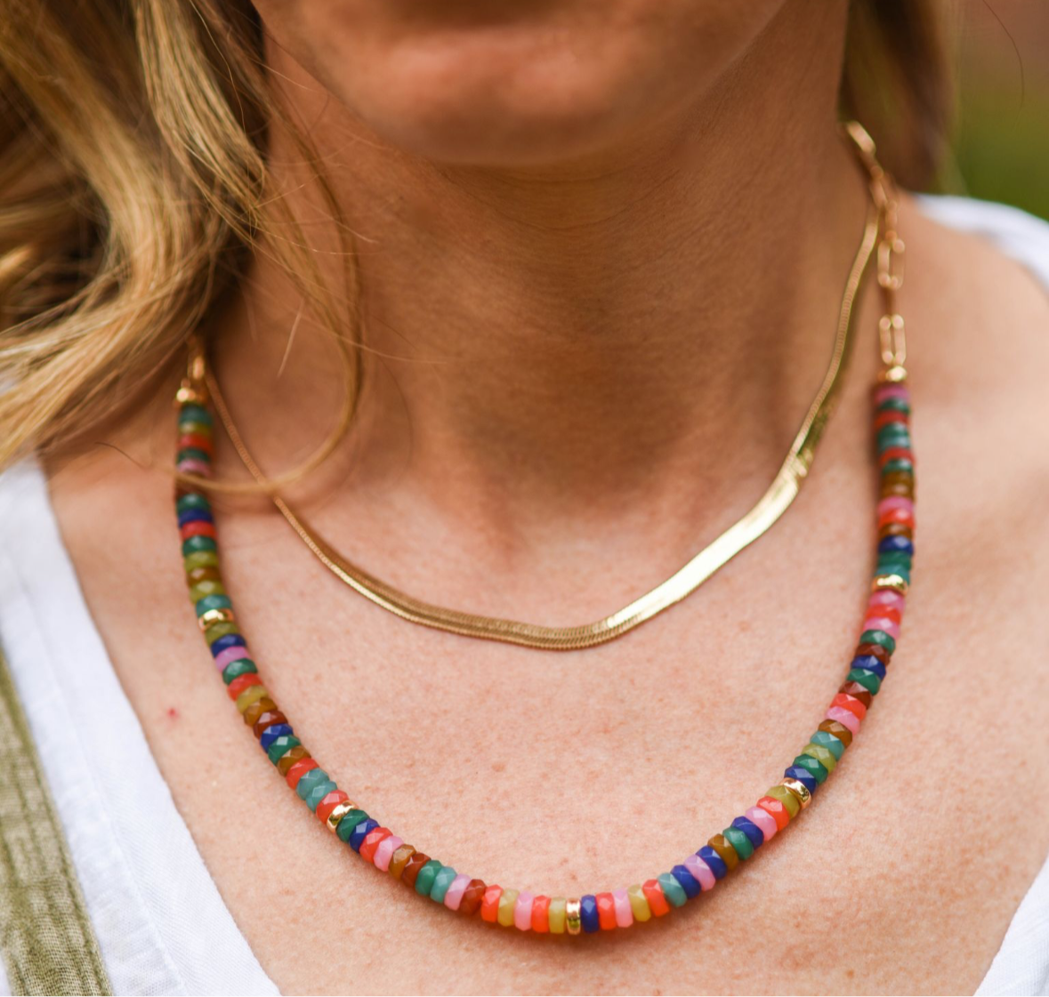 Picture of model wearing a short gold herringbone chain with a multicolored beaded necklace stacked beneath.