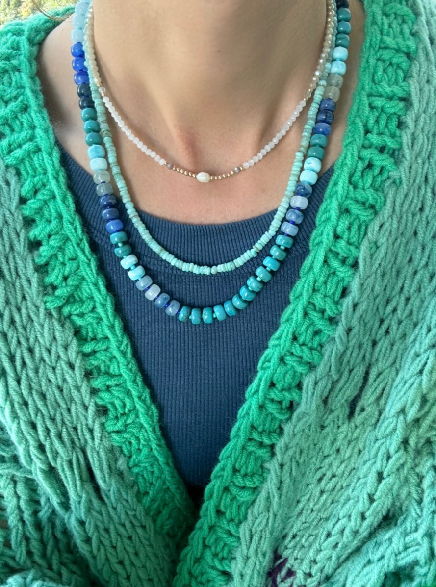 Picture of the front of a woman wearing a set of three bead necklaces. Necklace beads are blues and turquoise