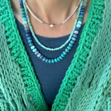 Picture of the front of a woman wearing a set of three bead necklaces. Necklace beads are blues and turquoise