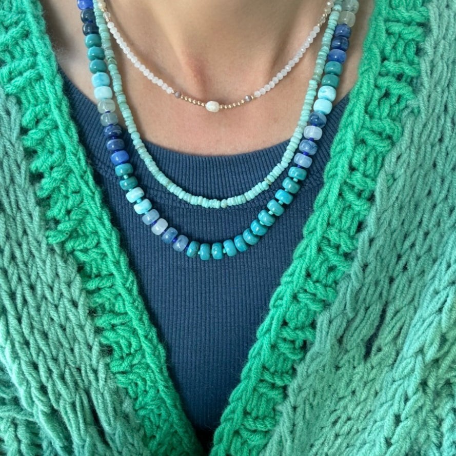Picture of the front of a woman wearing a set of three bead necklaces. Necklace beads are blues and turquoise