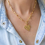 Girl wearing a necklace around her neck with a gold paperclip link chain with a heart medallion attached to it