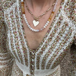 Picture of a woman's chest and dress wearing a set of stacked necklaces. One necklace has white beads and amber beads and one necklace with large gold links, a toggle clasp and with a gold heart charm.