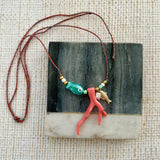 Picture of a woven string necklace with ocean themed beads on it. Main beads are a blue fish bead, a coral coral, a small freshwater Pearl pendant and a small gold fish pendant.
