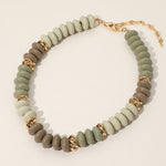 Necklace with green and brown beads and gold accents on a light beige background