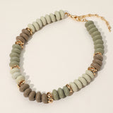 Necklace with green and brown beads and gold accents on a light beige background