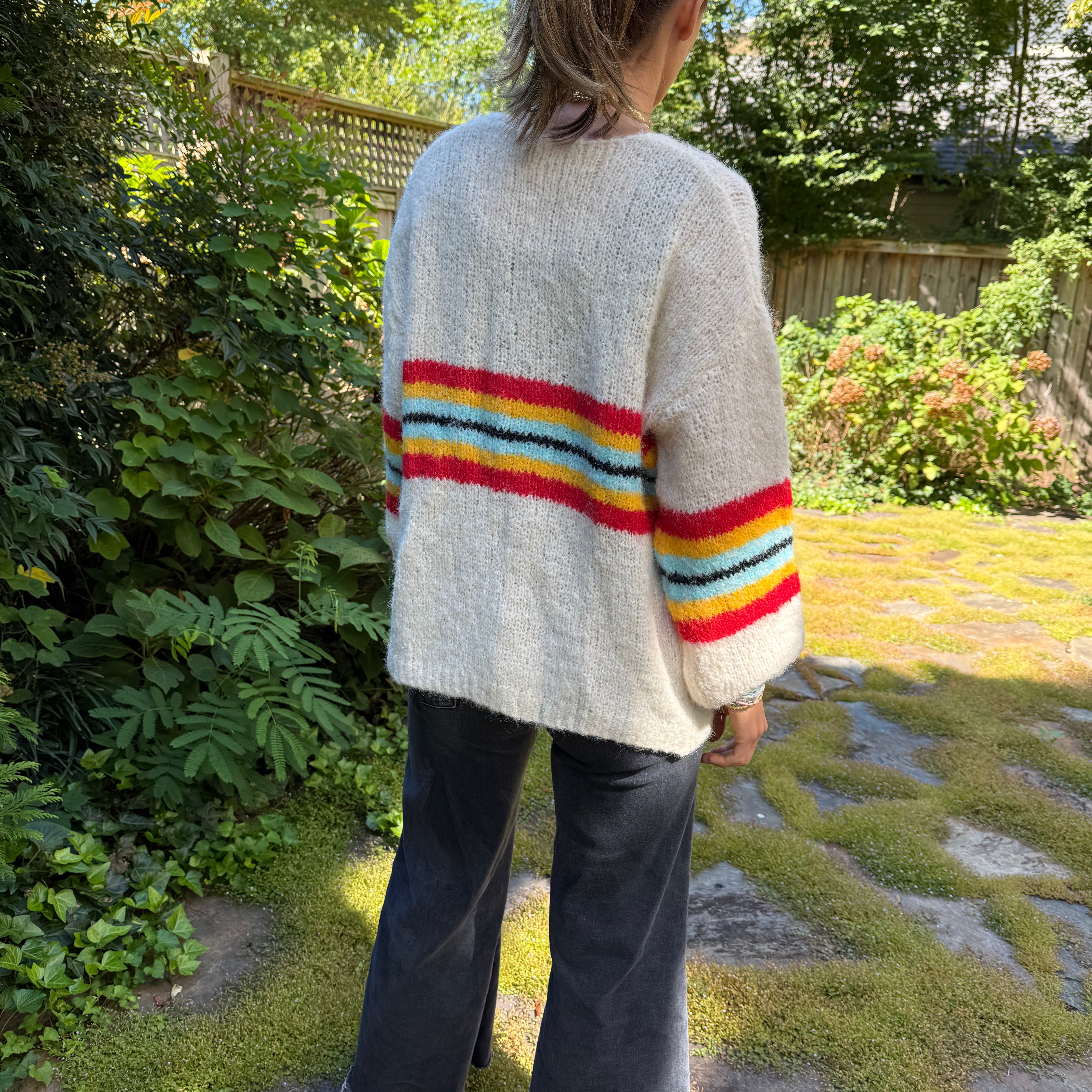 Person wearing a white sweater with a colorful striped design in a garden setting